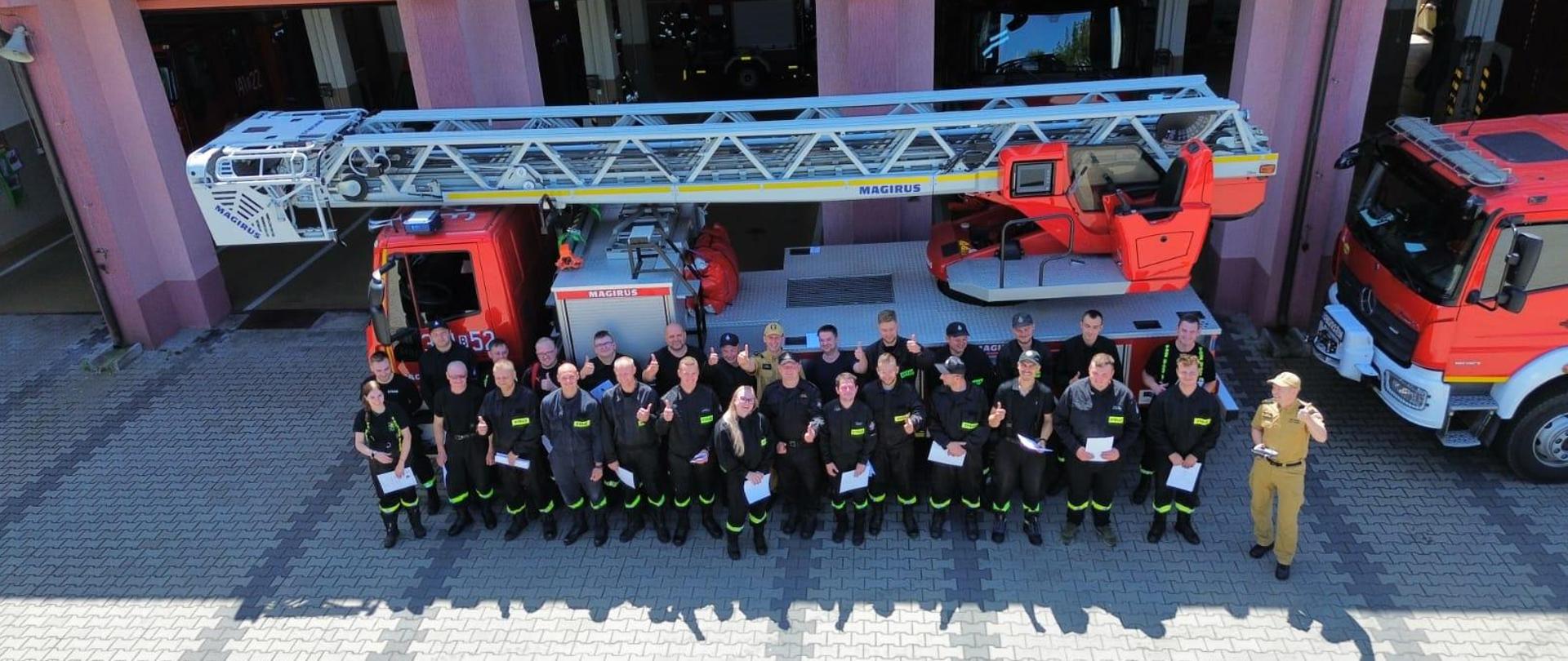 Na zdjęciu widać młodych strażaków strojących przed drabiną mechaniczną