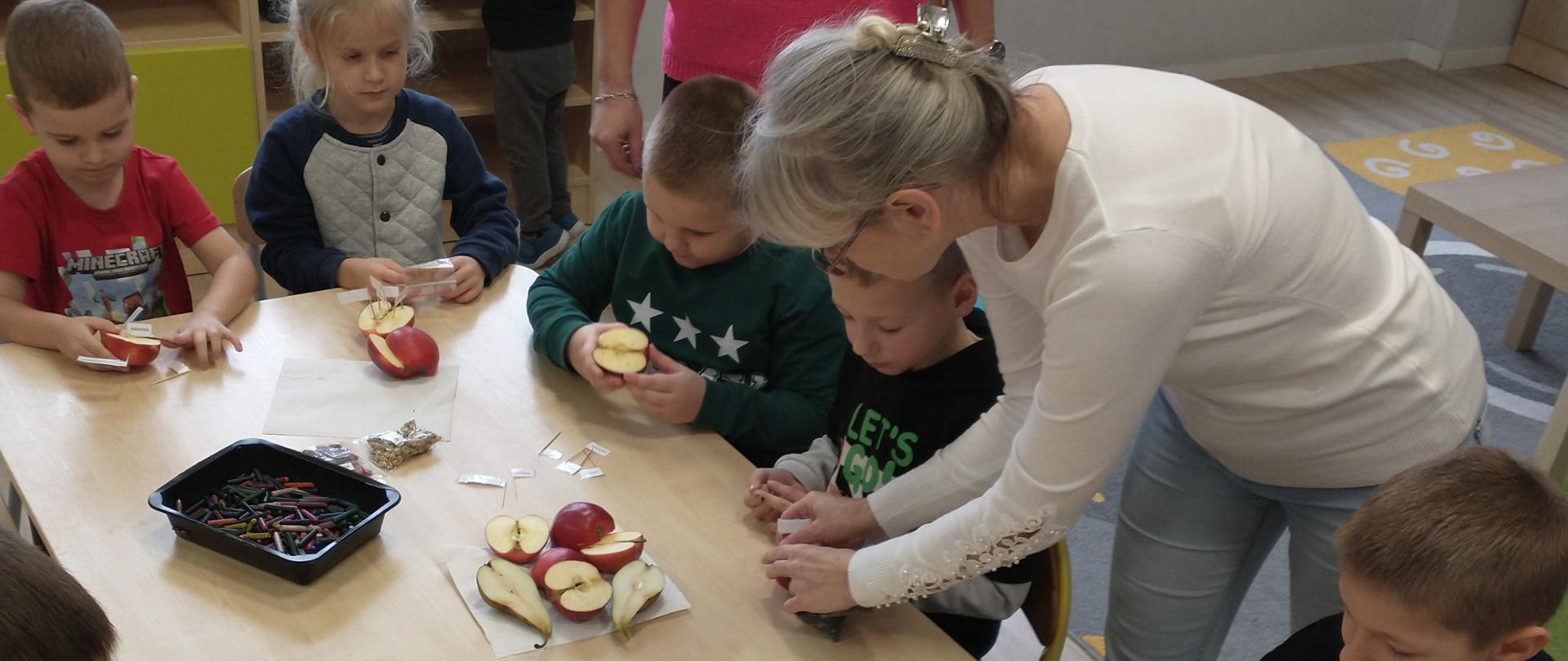 Dzieci siedzące przy stole na sali wraz z Inspektorem PIORiN trzymającym jabłko.