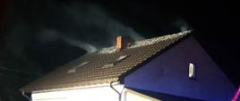 Na zdjęciu szczyt dachu budynku jednorodzinnego, z którego wydobywa się dym.