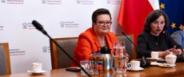 Na tle białej ścianki z napisami Ministerstwo Edukacji Narodowej oraz flag Polski i UE siedzi wiceminister Lubnauer i kobieta. 