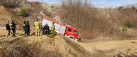 Kierowca w pojeździe pożarniczym ćwiczy jazdę w trudnym terenie, zjeżdża ze wzniesienia, strażacy obserwują