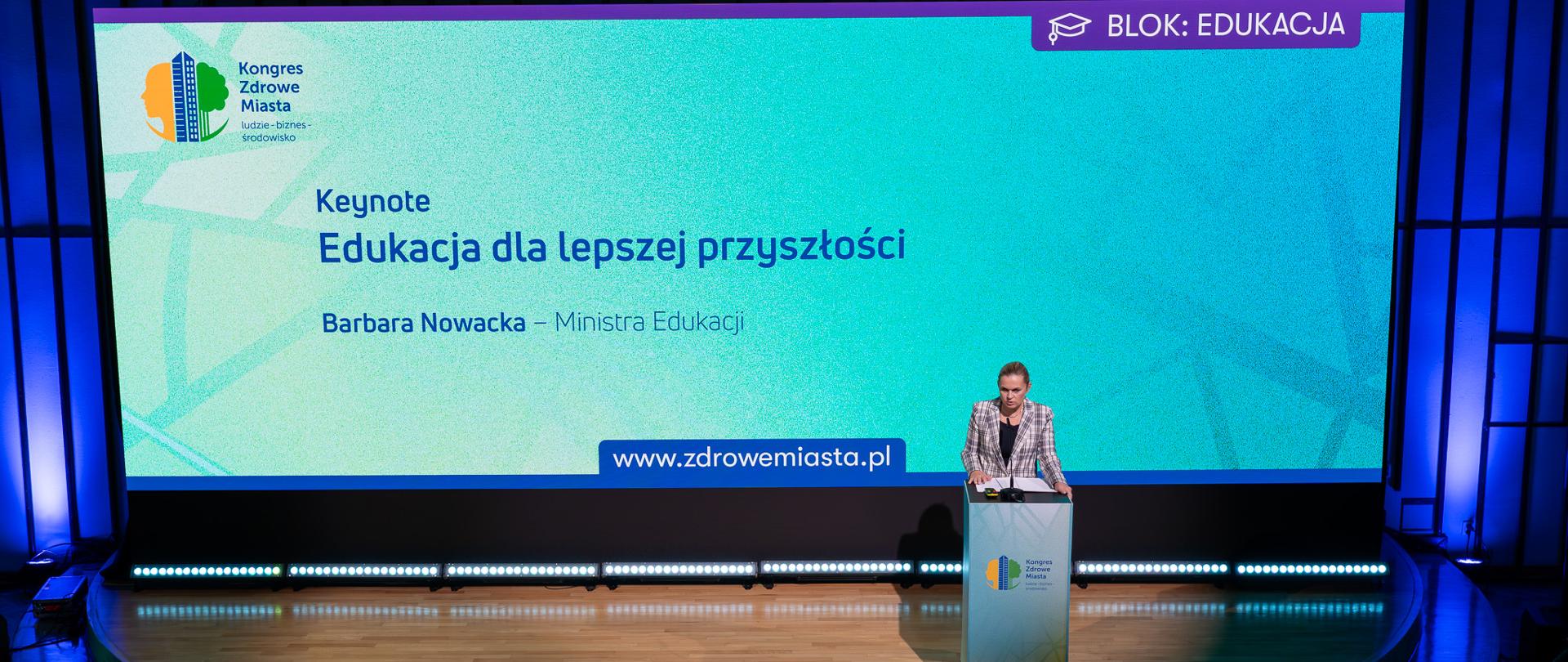 Widok z góry na scenę, na której przy mównicy stoi Minister Barbara Nowacka, w tle tuzy ekran na którym wyświetlany jest tytuł: Edukacja dla lepszej przyszłości oraz logo kongresu