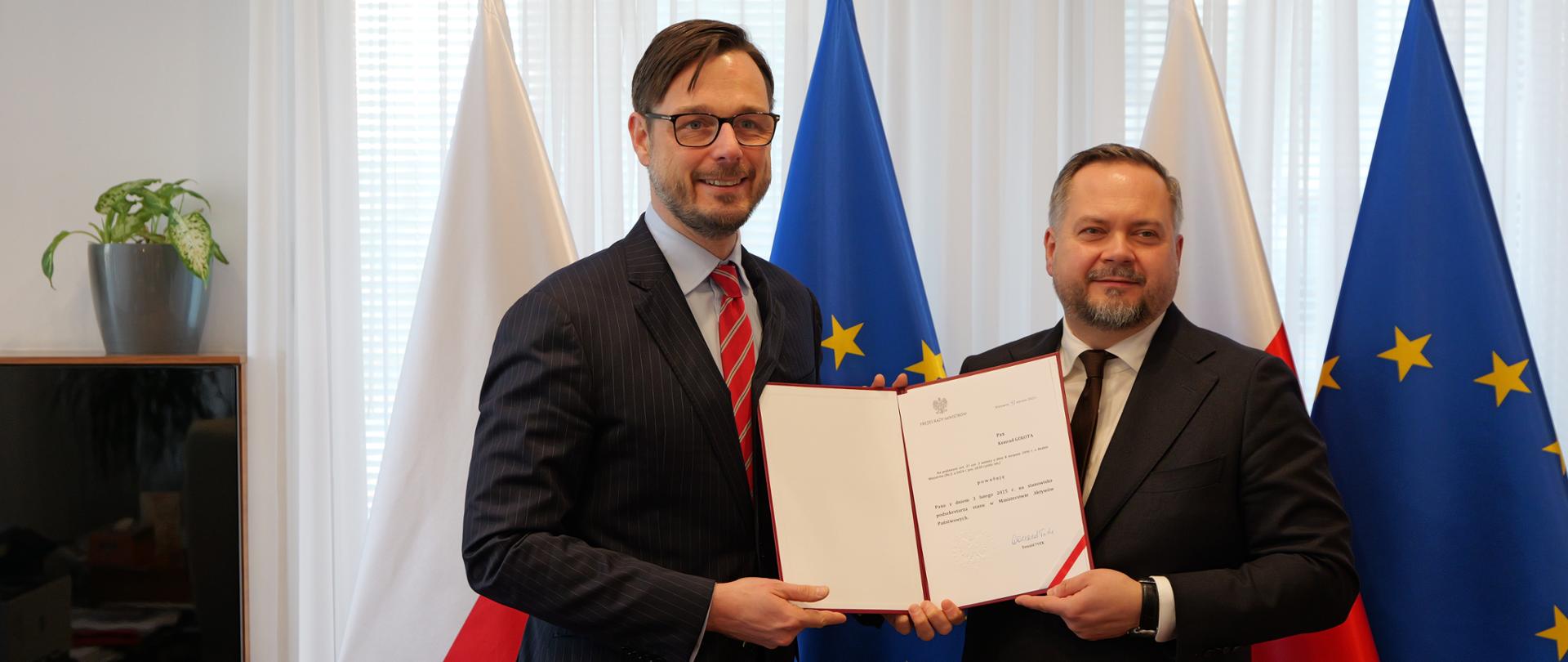 Minister Jakub Jaworowski i wiceminister Konrad Gołota stoją na tle flag - Polski i UE.