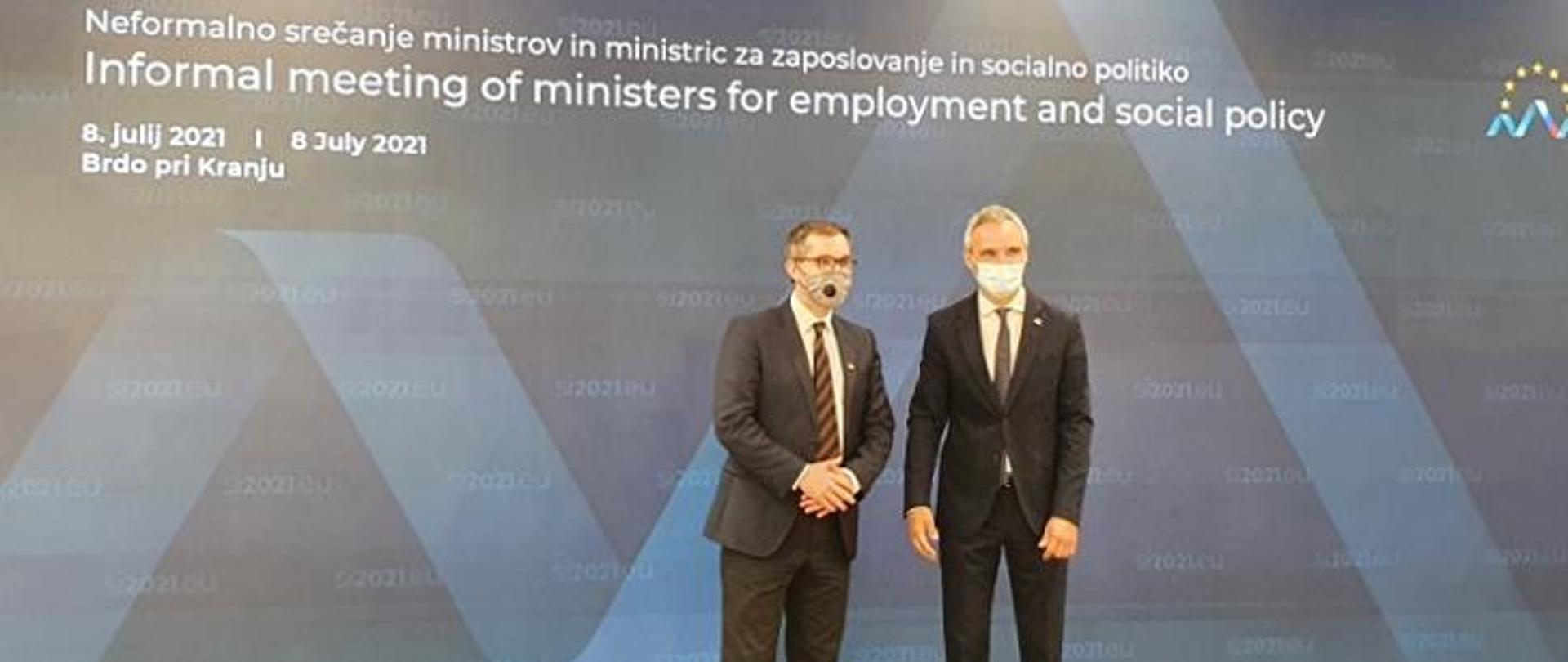 Deputy Minister of the Ministry of Labor and Social Policy, Marek Niedużak, standing in a mask against the background of a banner with an inscription "Informal meeting of ministers for employment and social policy"