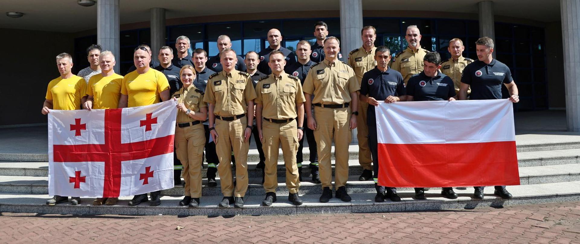 Pamiątkowe zdjęcie grupowe gruzińskich strażaków uczestniczących w ćwiczeniach ratownictwa wysokościowego w towarzystwie dwóch Zastępców Komendanta Centralnej Szkoły PSP, dwóch funkcjonariuszy CS PSP, funkcjonariuszki oraz dwóch funkcjonariuszy KG PSP, trzech instruktorów ratownictwa wysokościowego oraz tłumacza