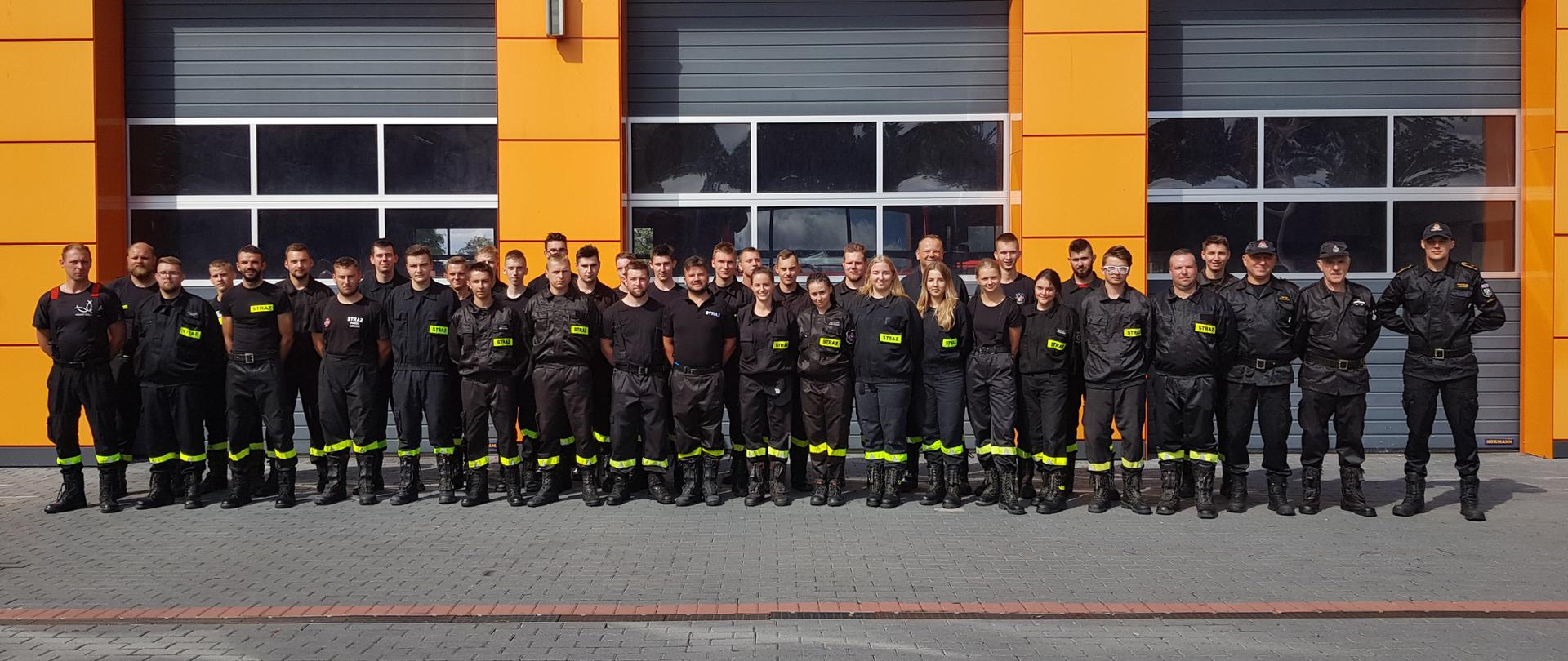 Pamiątkowe zdjęcie 36 kursantów, którzy chwilę temu pomyślnie ukończyli szkolenie podstawowe strażaków-ratowników OSP. Wraz z komisją egzaminacyjną, pozują w dwuszeregu przed bramami wyjazdowymi wolsztyńskiej jednostki.
