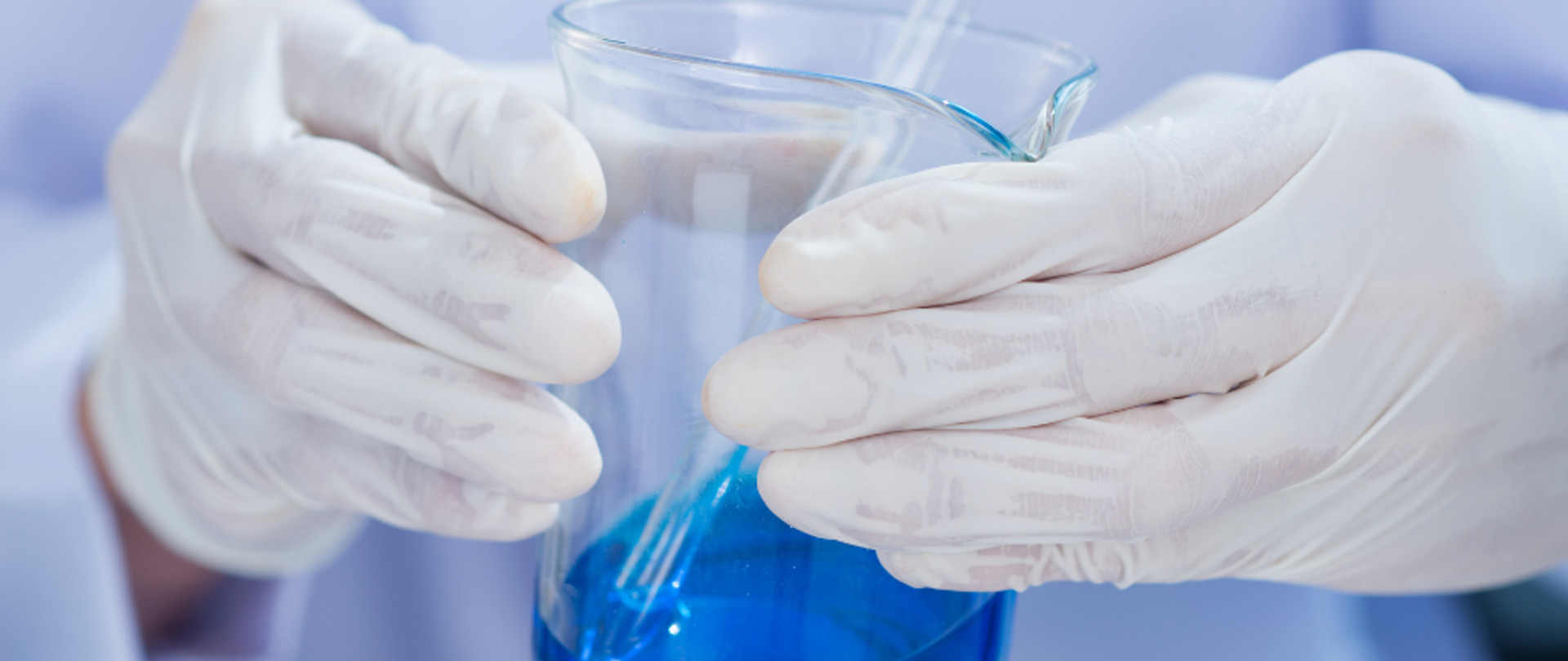 Osoba w rękawiczkach trzyma zlewkę laboratoryjną wypełnioną niebieską substancją