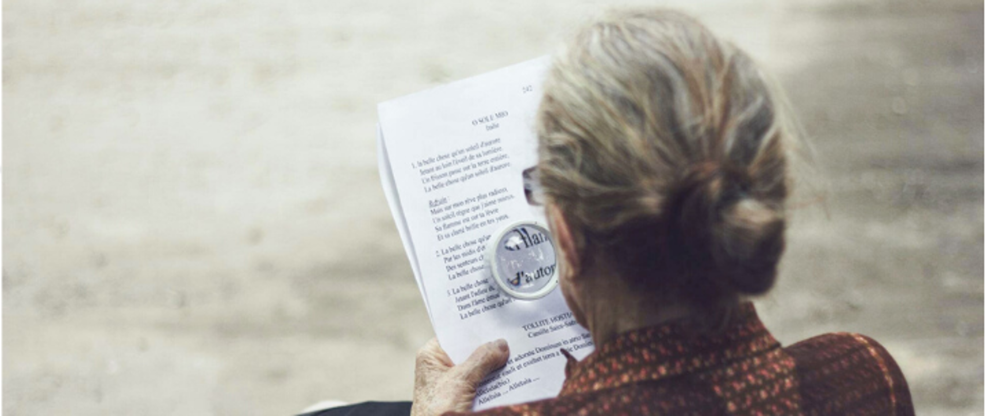 Zdjęcie starszej pani siedzącej i czytającej dokument pod lupą. W rogach loga GovTech, Polskiej Agencji Prasowej i napius #ZwalczWirusaKodem oraz #FakeHunter.