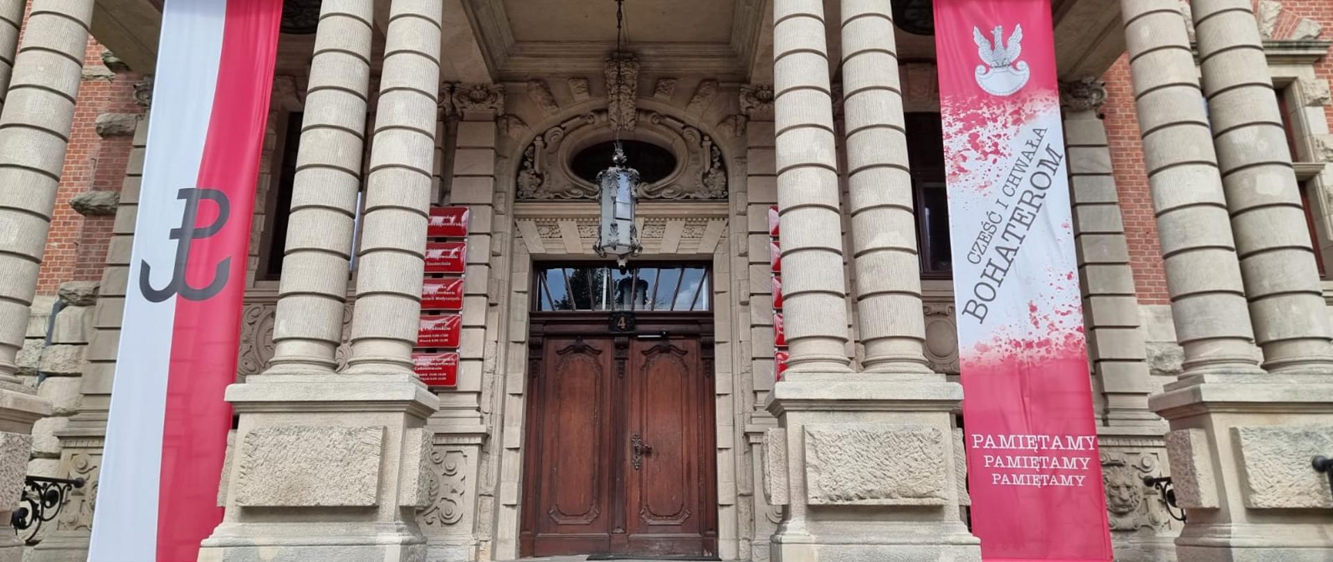 po lewej stronie od wejścia do budynku ZUW baner z symbolem Polski Walczącej na biało-czerwonym tle, po prawej napis Cześć i chwała Bohaterom, Pamiętamy