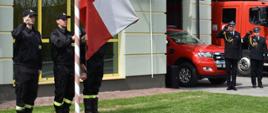 Strażacy z JRG PSP w Pińczowie podnoszą flagę państwową na maszt. Komendant Powiatowy PSP z Zastępcą Komendanta Powiatowego PSP salutują.
