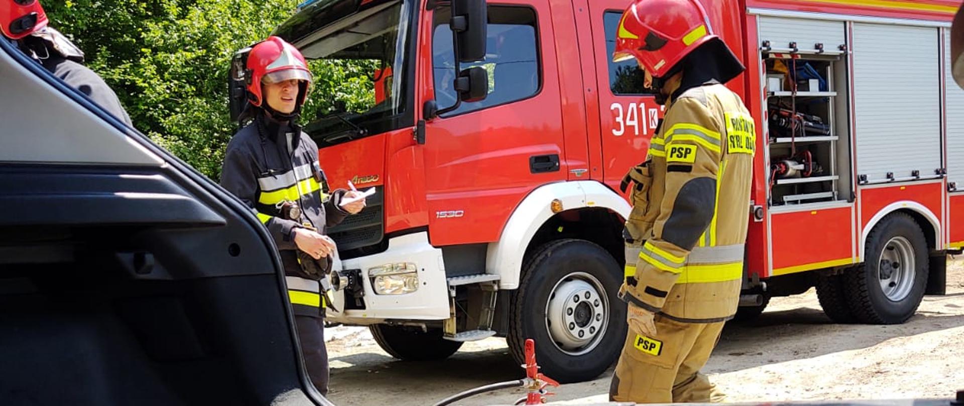 Miejsce pożaru we wnętrzu samochodu. Poza samochodem strażacy oraz samochód pożarniczy.