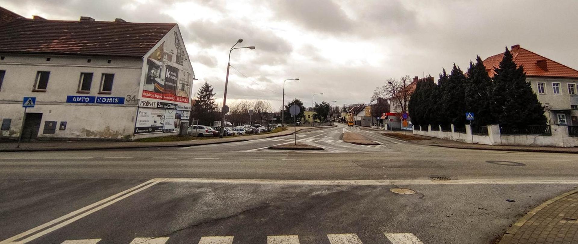 Fotografia z poziomu terenu na skrzyżowanie dróg w Raciborzu. W pierwszym planie widoczne przejście dla pieszych, w środkowym droga przycinająca teren w poprzek, w dalszym droga skanalizowana z pozostałymi wydzielonymi wyspami separacyjnymi. 