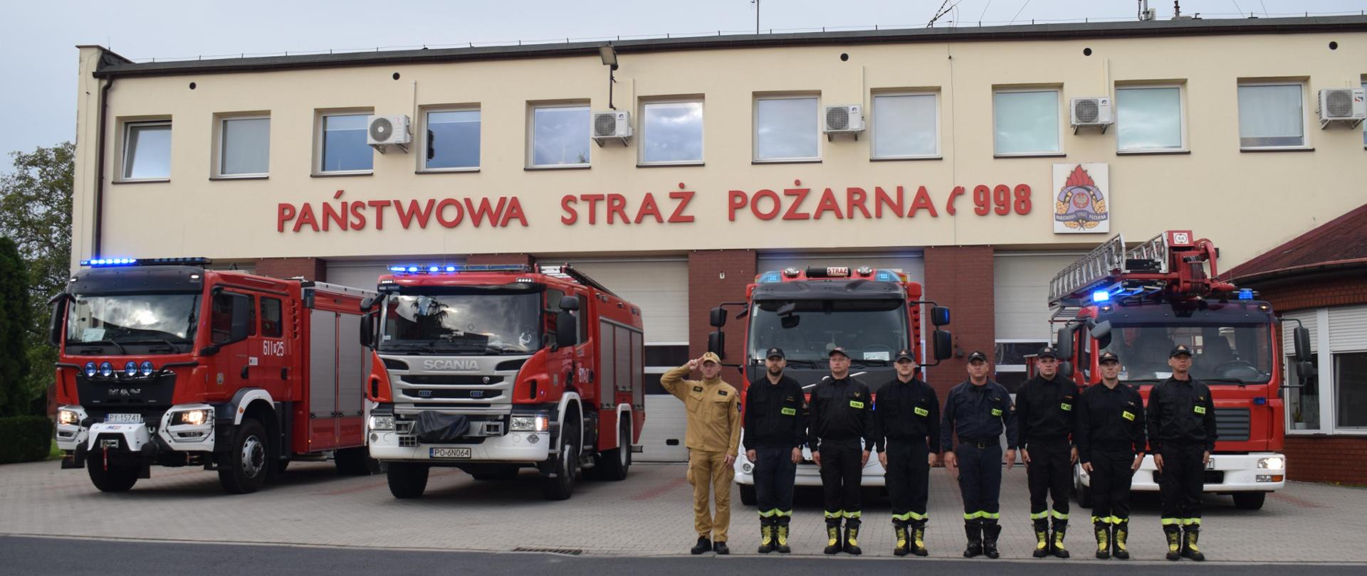 Strażacy podczas oddawania hołdu tragicznie zmarłym podczas służby kolegom. W tle samochody pożarnicze z włączonymi sygnałami świetlnymi i dźwiękowymi.