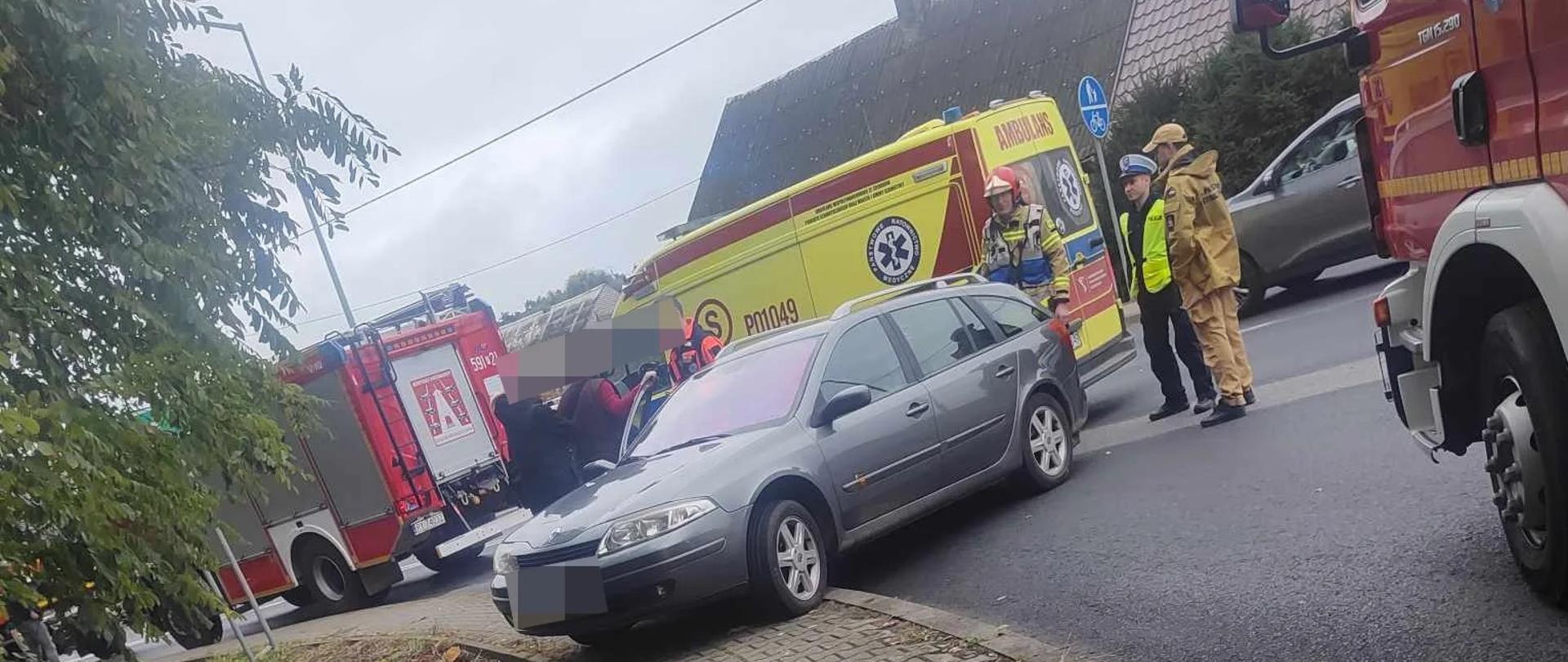 Samochód na drodze i chodniku, w pobliżu samochody strażackie i karetka