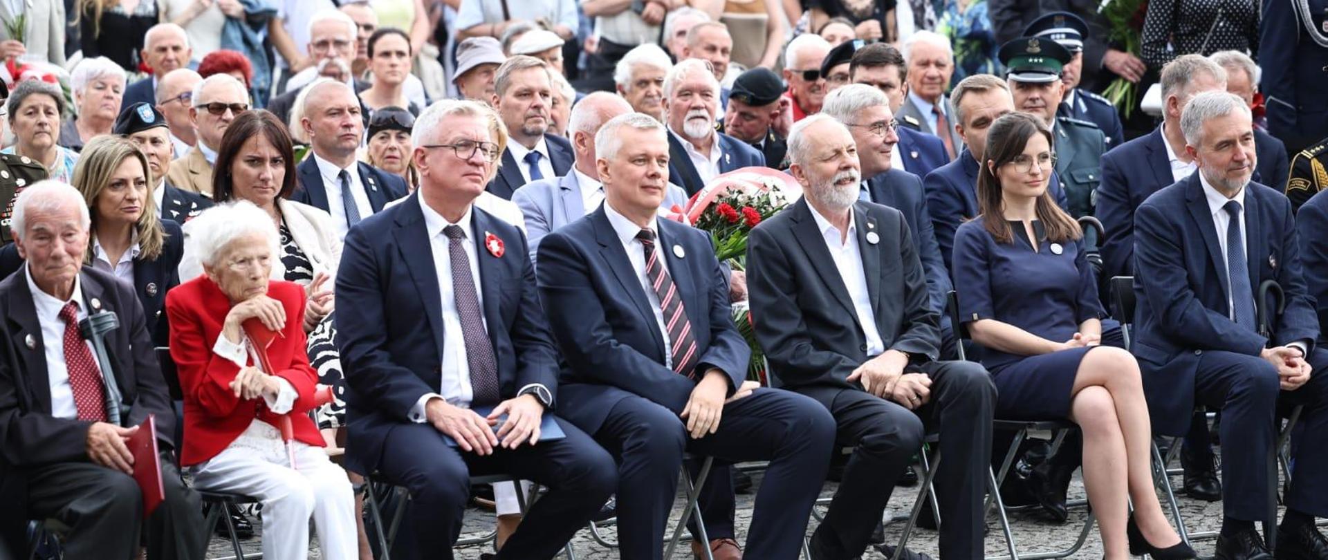 Grupa osób siedzi na krzesłach w kilku rzędach. W pierwszym minister Tomasz Siemoniak, obok niego prezydent Poznania Jacek Jaśkowiak i senator Rafał Grupiński. 