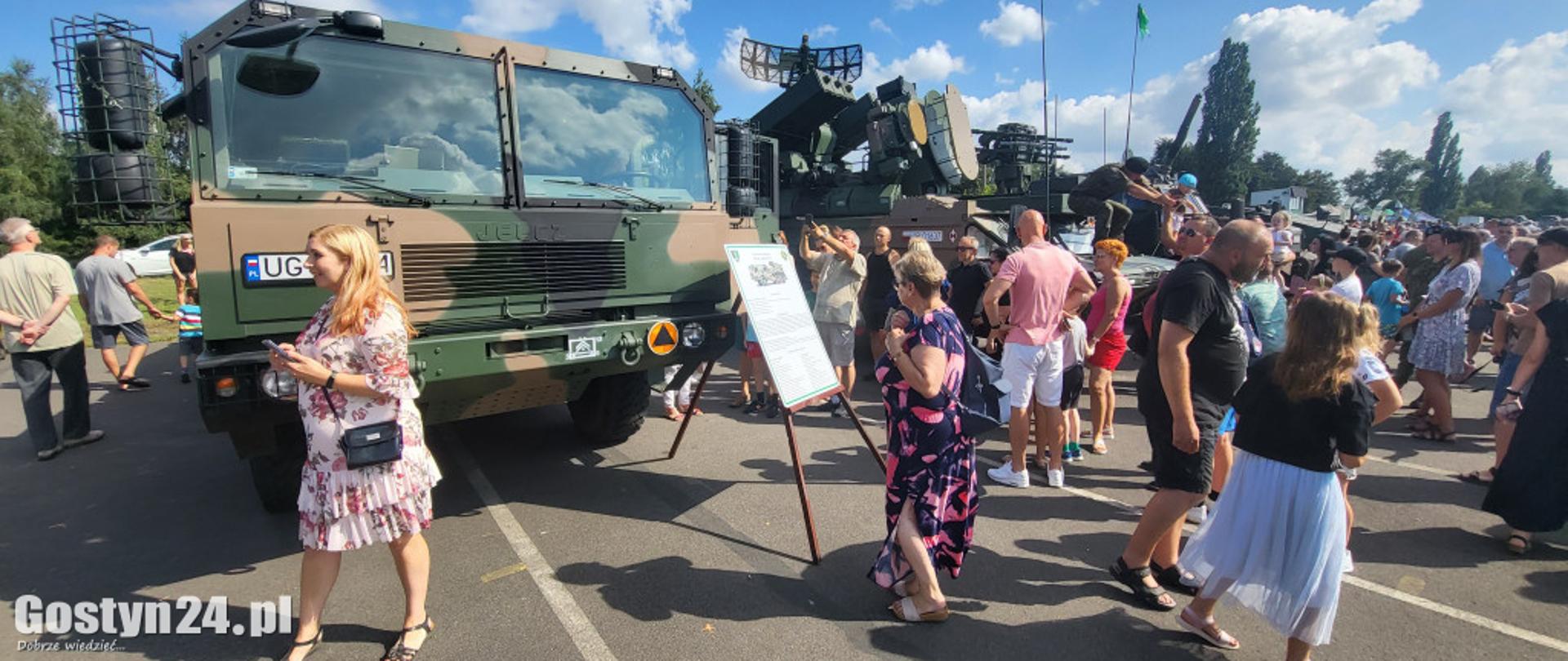 Zdjęcie przedstawia pojazdy wojskowe i odwiedzających ludzi.