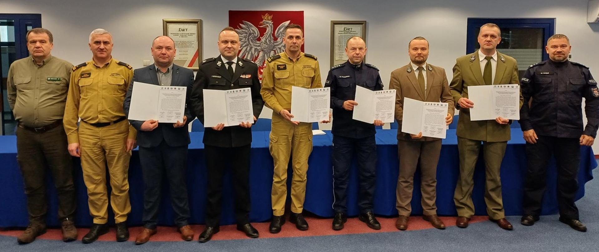 Na zdjęciu w sali konferencyjnej Komendy Powiatowej Policji w Gorlicach widoczni przedstawiciele służb mundurowych i instytucji z powiatu gorlickiego trzymający w rękach podpisany apel służb powiatu gorlickiego dotyczący niewypalania traw. 