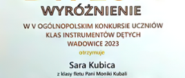 Baner na białym tle z napisem "Wyróżnienie w V Ogólnopolskim Konkursie Uczniów Klas Instrumentów Dętych, Wadowice 2023 otrzymuje Sara Kubica z klasy fletu Pani Moniki Kubali"