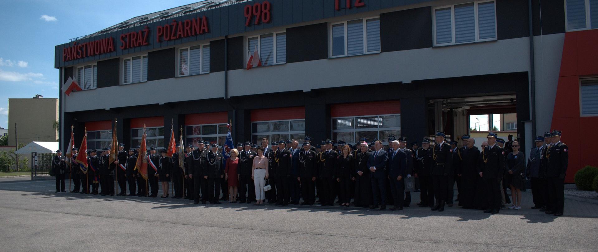 Na zdjęciu widać na tle budynku JRG w Sandomierzu około 100 osób stojących w szeregu - cywili i mundurowych oraz poczty sztandarowe, osoby widoczne na zdjęciu brały udział w uroczystości. Zdjęcie ma charakter pamiątkowy. Na budynku widnieje napis Straż Pożarna 998 112.