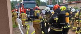 Zdjęcie przedstawia strażaków w sprzęcie ochrony układu oddechowego podczas ewakuacji poszkodowanego z budynku objętego pożarem.