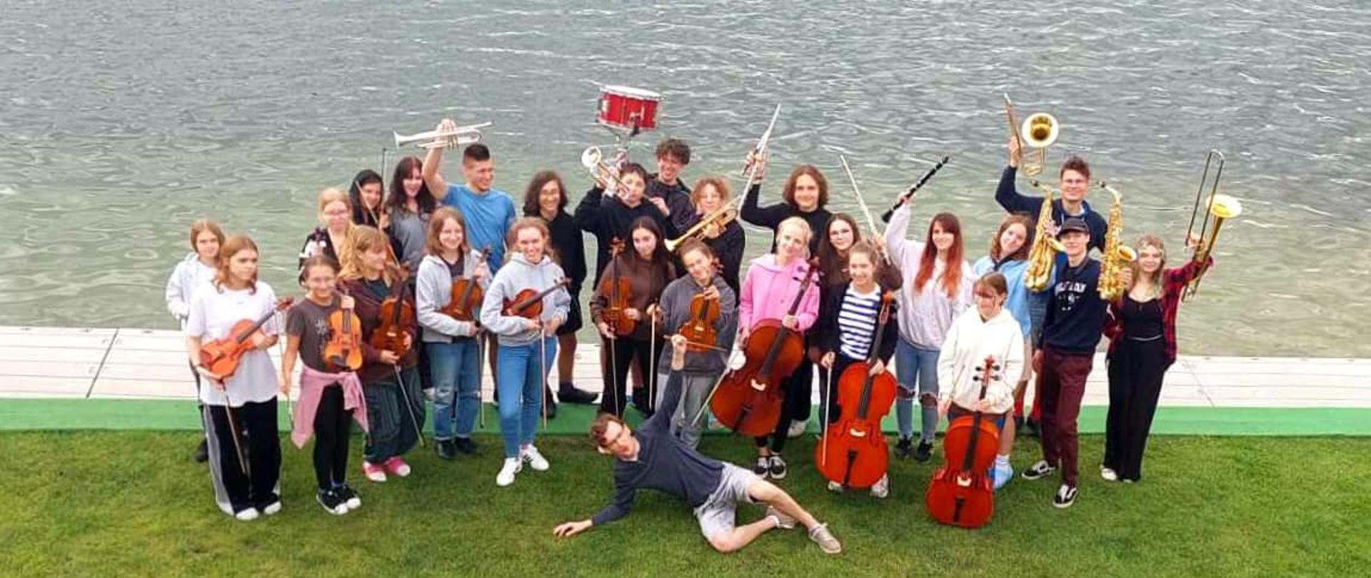 Zdjęcie - na tle jeziora grupa młodzieży z instrumentami - orkiestra
