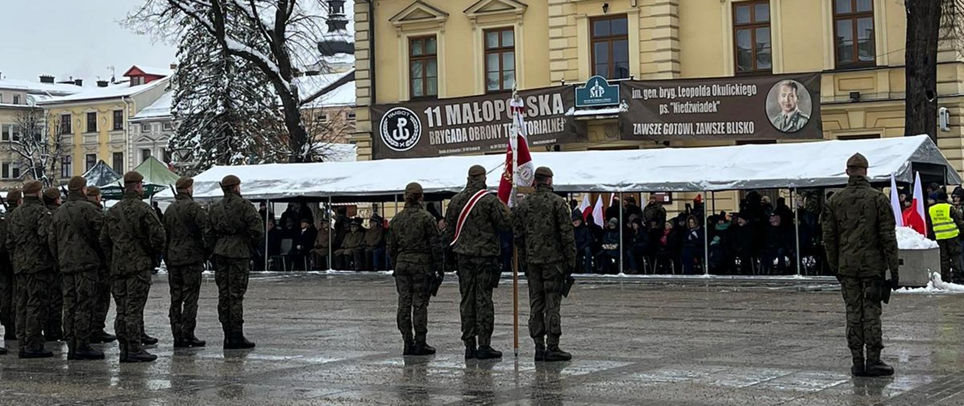 Rynek w Nowym Tartu. Na zdjęciu widziany od tyłu poczet sztandarowy oraz kompania żołnierzy ubranych w wojskowe mundury.