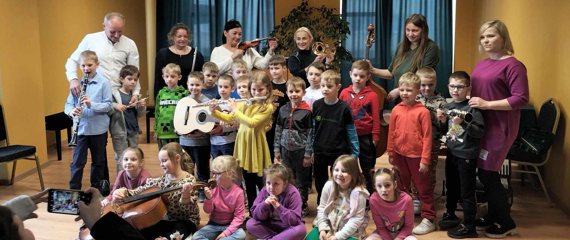 Na fotografii widzimy wszystkich uczestników koncertu. Młodzież szkolną i publiczność, wszyscy uśmiechają się.