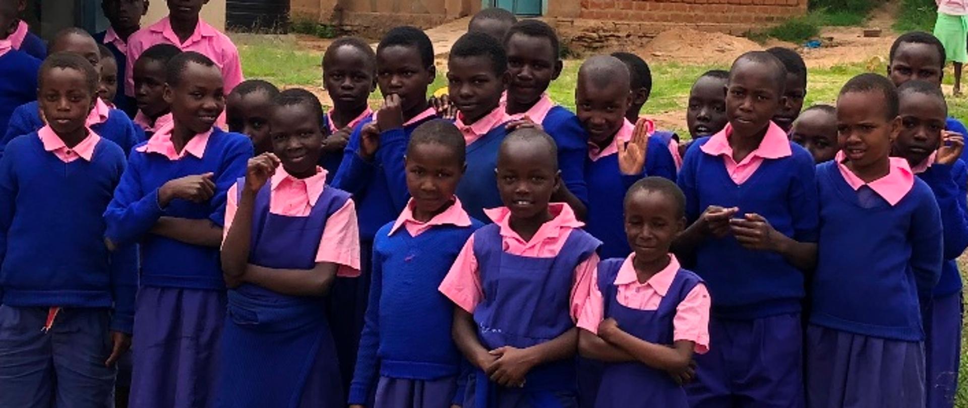 Uśmiechnięte kenijskie dzieci w niebieskich mundurkach przed szkołą
