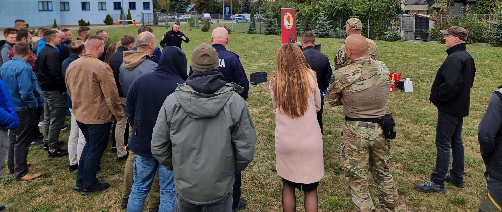 Plac pomiędzy budynkami, w głębi funkcjonariusz CS PSP prowadzący pokaz, wokół stojący zebrani obserwatorzy wydarzenia