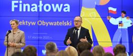 Minister Nowacka i minister Bodnar stoją na tle dużego ekranu z napisem Gala finałowa konkursu Obiektyw Obywatelski. przed nimi na krzesłach siedzą ludzie i słuchają.