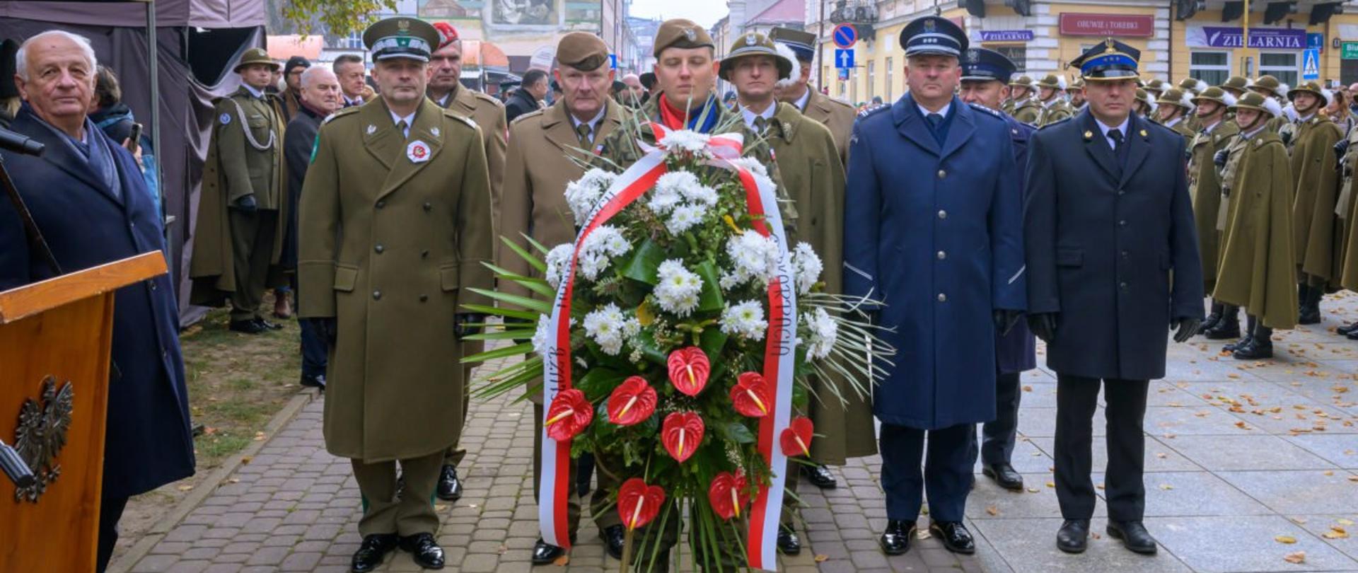 Zdjęcie zrobione na zewnątrz podczas uroczystych obchodów Narodowego Święta Niepodległości w Rzeszowie. Delegacja przedstawicieli służb mundurowych składa kwiaty pod pomnikiem Marszałka Piłsudskiego. Oficerowie stoją na baczność i salutują. Delegacji znajdują się oficerowie Wojska Polskiego, Policji, Państwowej Straży Pożarnej, Straży Granicznej, Służby Więziennej