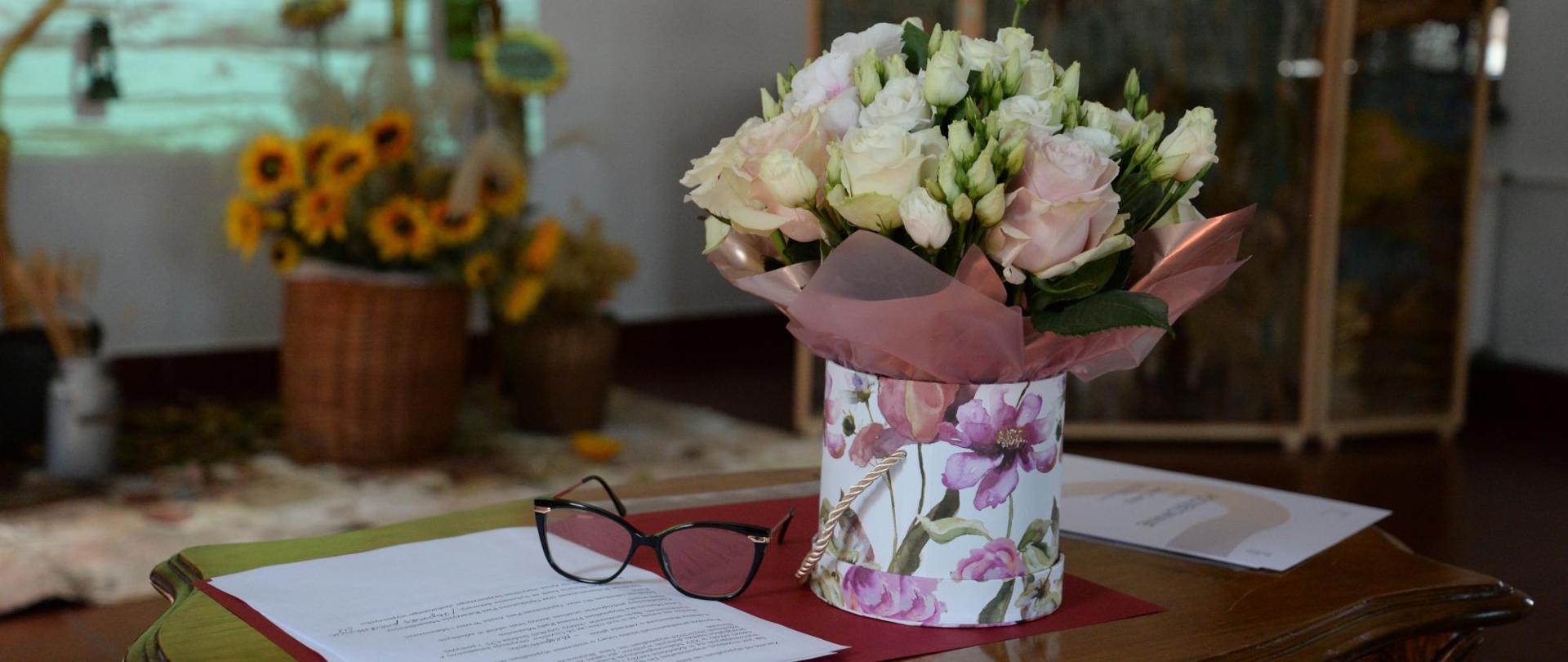 na stoliku bukiet kwiatów, obok okulary i dyplom