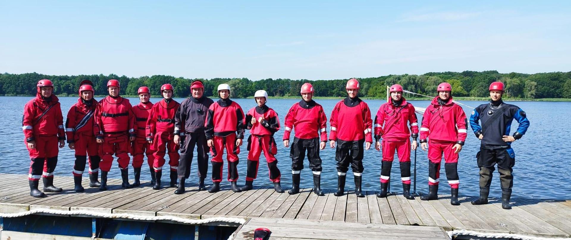 Szkolenie z ratownictwa na obszarach wodnych realizowanego przez ksrg w zakresie podstawowym. Na zdjęciu strażacy podczas szkolenia na jeziorze, strażacy stoją do zdjęcia pamiątkowego, ubrani w skafandry nurkowe.