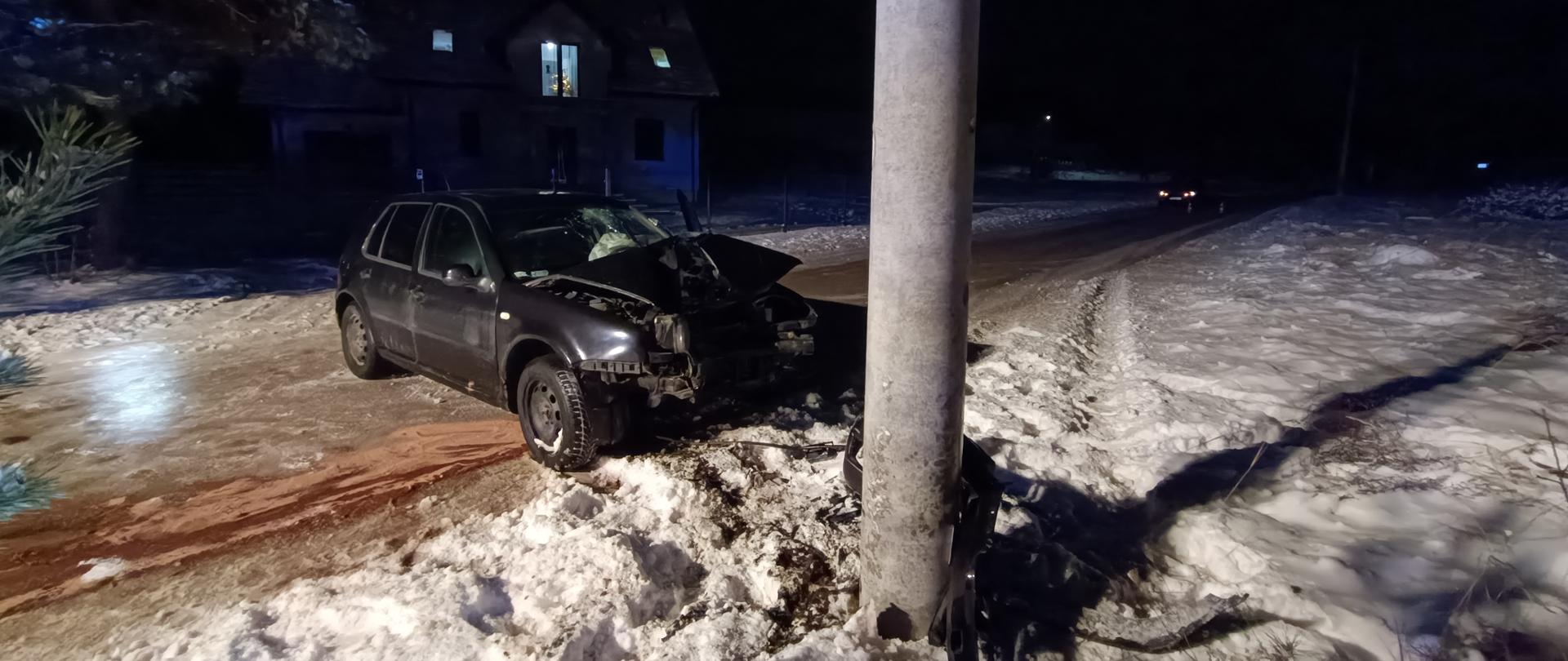 Zdjęcie przedstawia zniszczony w wyniku zderzenia samochód osobowy stojący przed betonowym słupem w który uderzył