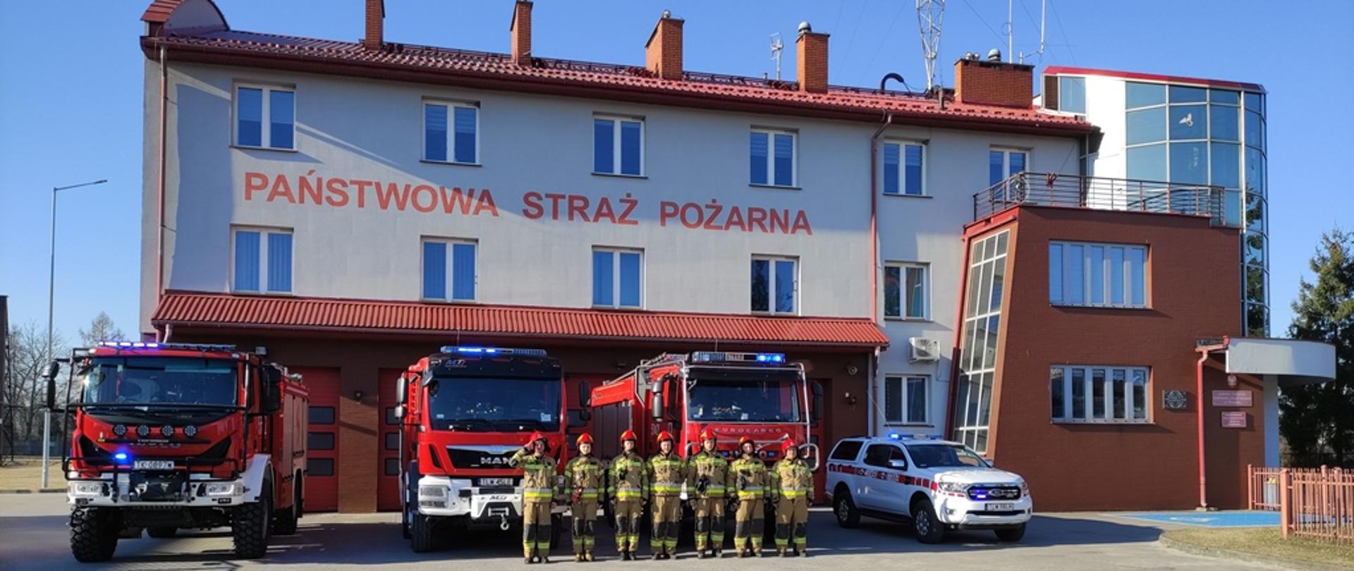 Zmiana służby w JRG Włoszczowa, zmiany służbowe ustawione w szeregu przed pojazdami pożarniczymi przed budynkiem Komendy Powiatowej Państwowej Straży Pożarnej we Włoszczowie