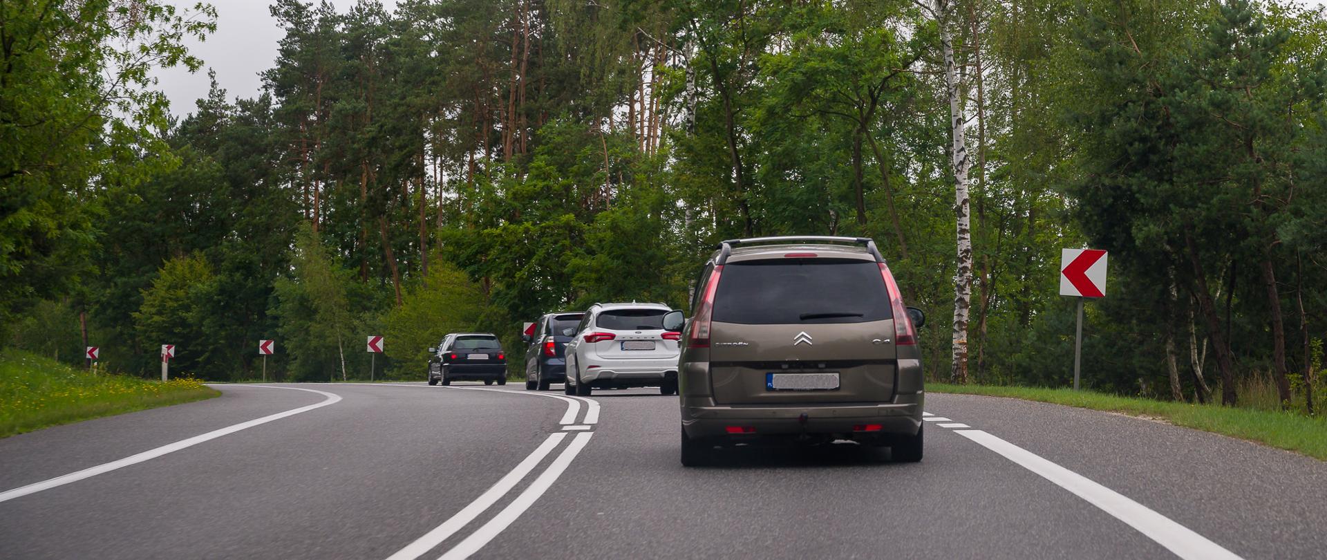 Pojazdy jadące drogą krajową. Zbliżają się do zakrętu w lewo.