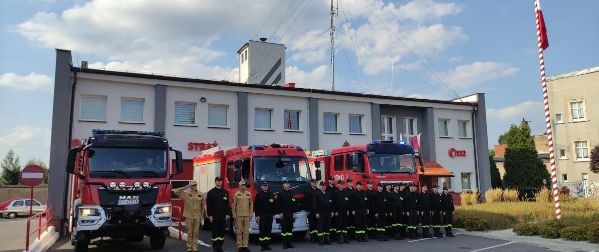 Zdjęcie przedstawia strażaków stojących przed wozami bojowymi podczas oddawania hołdu powstańcom warszawskim