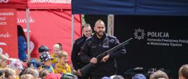 Policjant na stanowisku edukacyjnym prezentuje broń jaką dysponują policjanci