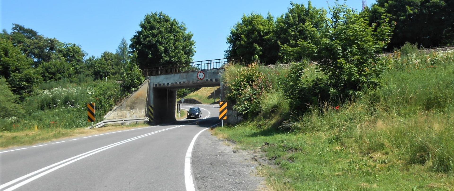 Zdjęcie przedstawia drogę krajową nr 55 w Brachlewie z samochodem osobowy przy wiadukcie z linią kolejową nr 207. Skrajnia drogi jest ograniczona Istniejącym wiaduktem, który jest zbyt wąski i niski, by przejeżdżały nim samochody ciężarowe.