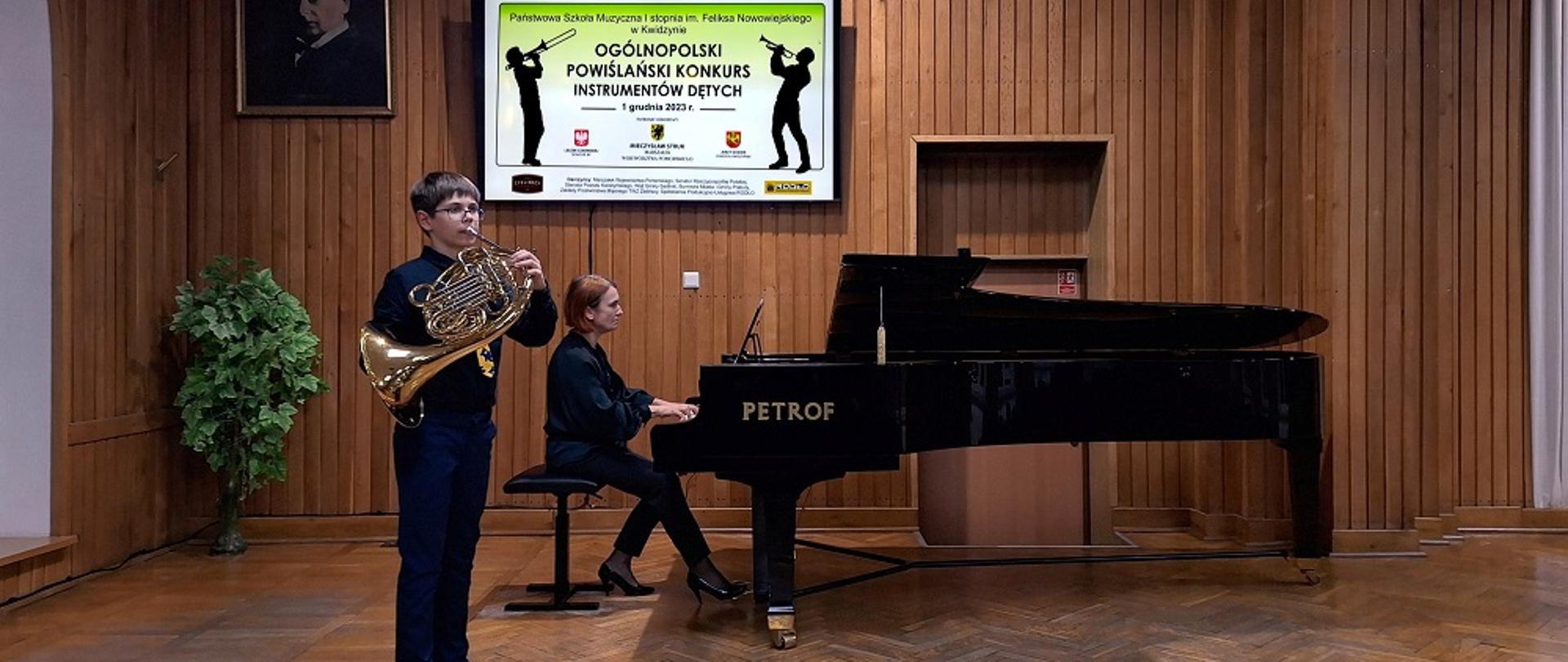 Uczeń gra na waltorni, akompaniuje przy fortepianie nauczycielka