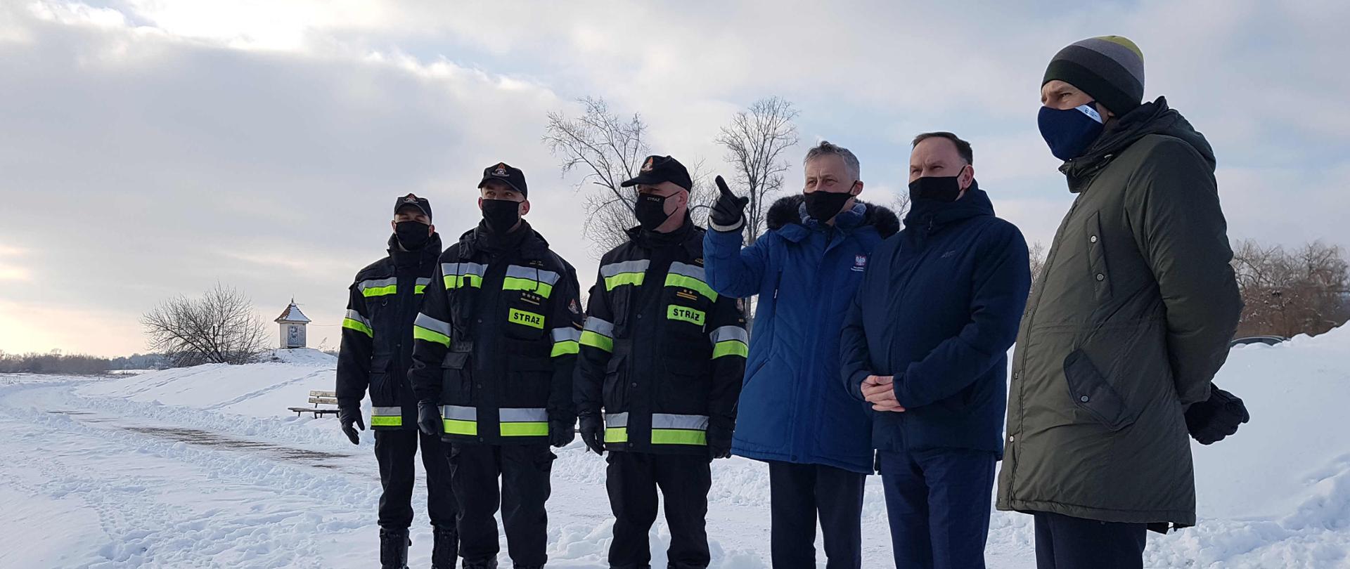 Zdjęcie zrobione na ośnieżonym brzegu rzeki Wisły na bulwarze im. Józefa Piłsudskiego w Sandomierzu. Na zdjęciu widać Wojewodę Świętokrzyskiego Zbigniewa Koniusza, Posła na Sejm RP Marek Kwitek, dyrektor Zarządu Zlewni Wód Polskich w Sandomierzu Pan Krzysztof Sobecki, Zastępca Świętokrzyskiego Komendanta Wojewódzkiego Państwowej Straży Pożarnej w Kielcach bryg. Grzegorz Rajca, Komendant Powiatowy Państwowej Straży Pożarnej w Sandomierzu st. kpt. Piotr Krytusa wraz ze swoimi pracownikami. Wojewoda zapoznaje się z aktualną sytuacja pogodową na rzece Wisła i Koprzywianka. 