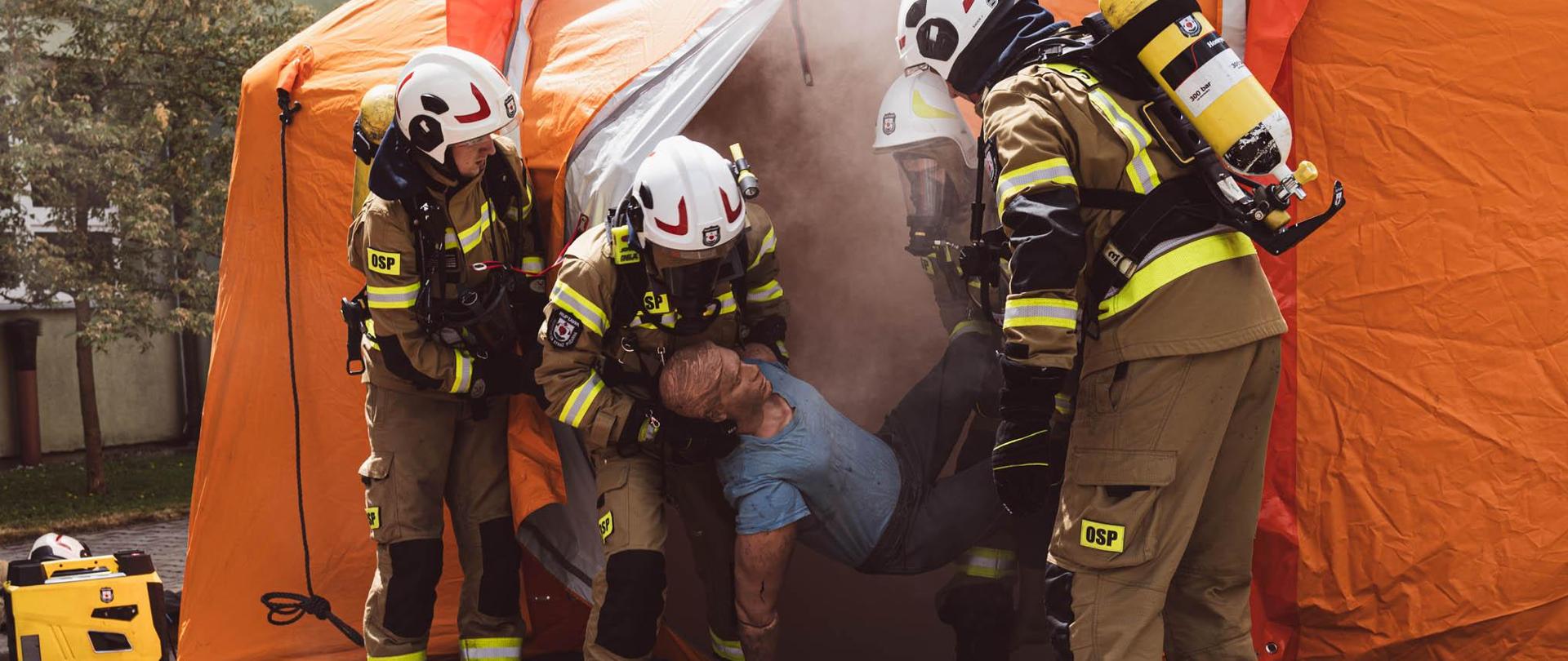 Strażacy w ramach zawodów OSP - ewakuują osobę poszkodowaną z zadymionego pomieszczenia (namiot).
