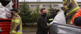 Zdjęcie przedstawia starostę jędrzejowskiego- Pana Pawła Farynę, który przy pomocy strażaków przekłada pakiety żywnościowe na samochód operacyjny ochotniczej straży pożarnej.