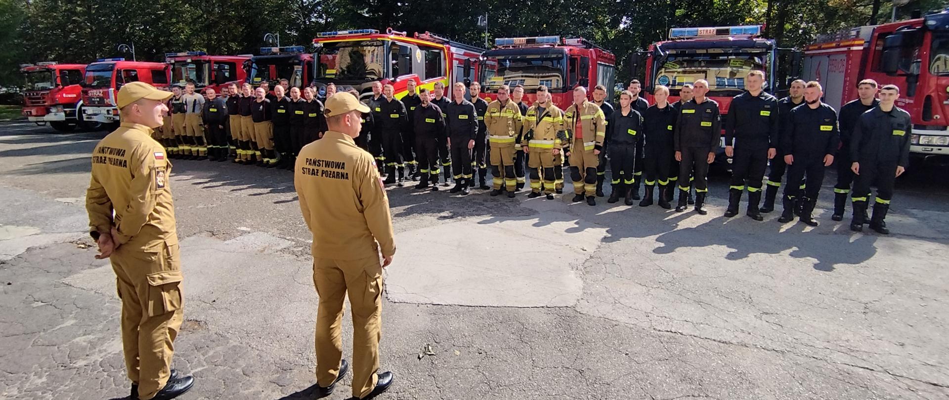 Widok z przodu. Zbiórka pododdziału na placu apelowym KP PSP w Wadowicach. Tyłem, a frontem do pododdziału stoi od lewej dowódca kompanii oraz zastępca komendanta powiatowego. 