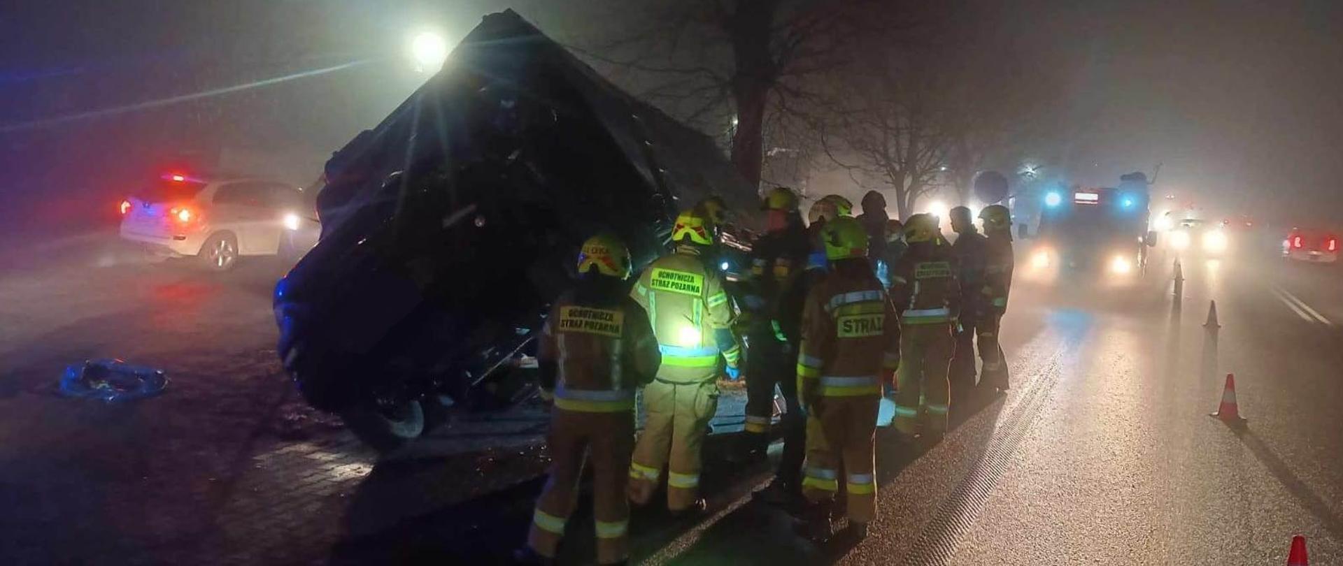 Przechylony samochód ciężarowy w rowie, jest ciemno, w pobliżu strażacy