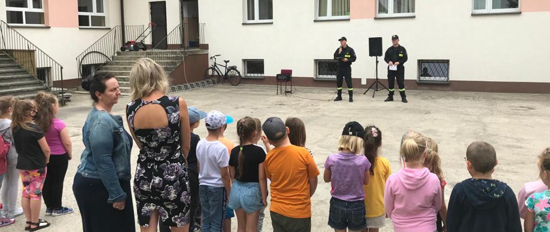 Zdjęcie przedstawia strażaków podczas prelekcji na temat akcji "Bezpieczne wakacje", przed strażakami znajduję się grupka dzieci.