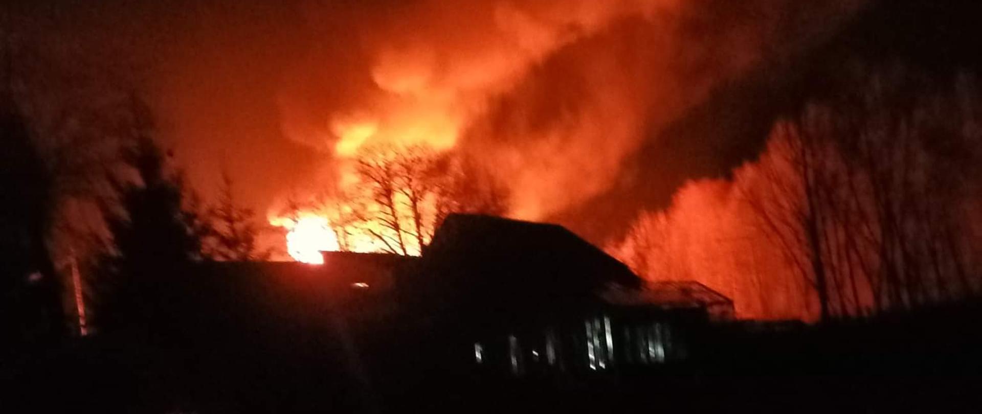 Na zdjęciu widoczny jest płonący budynek. Zdjęcie jest zrobione w nocy. W tle widać płomienie i kłęby dymu.