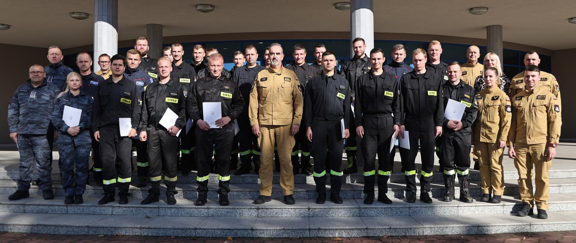 Pamiątkowe zdjęcie grupowe funkcjonariuszy PSP oraz straży marszałkowskiej będący uczestnikami szkolenia ratownictwa chemicznego i ekologicznego (25 osób) w towarzystwie Zastępcy Komendanta Centralnej Szkoły PSP, kobiety oraz funkcjonariuszki i czterech funkcjonariuszy CS PSP