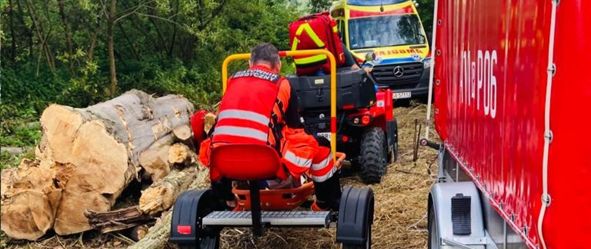 Na zdjęciu widoczne otoczenie lasu oraz quad Państwowej Straży Pożarnej transportujący osobę poszkodowaną do karetki pogotowia 