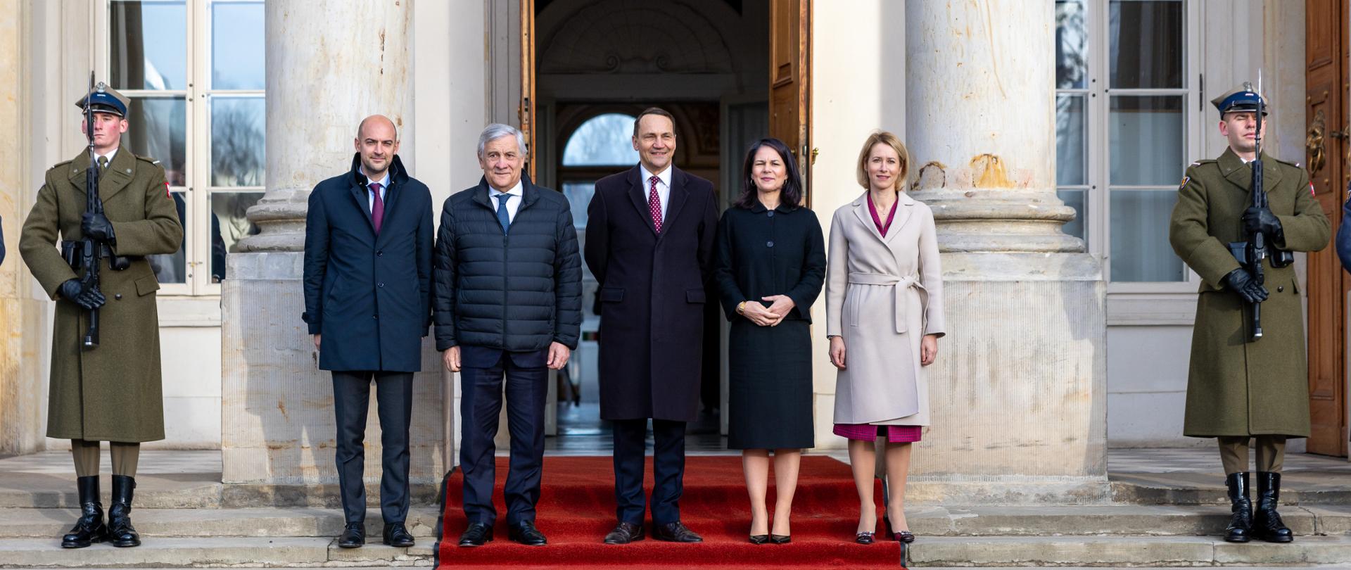 Na zdjęciu, na czerwonym dywanie, stoi pięć osób. W tle zabytkowy pałacyk.